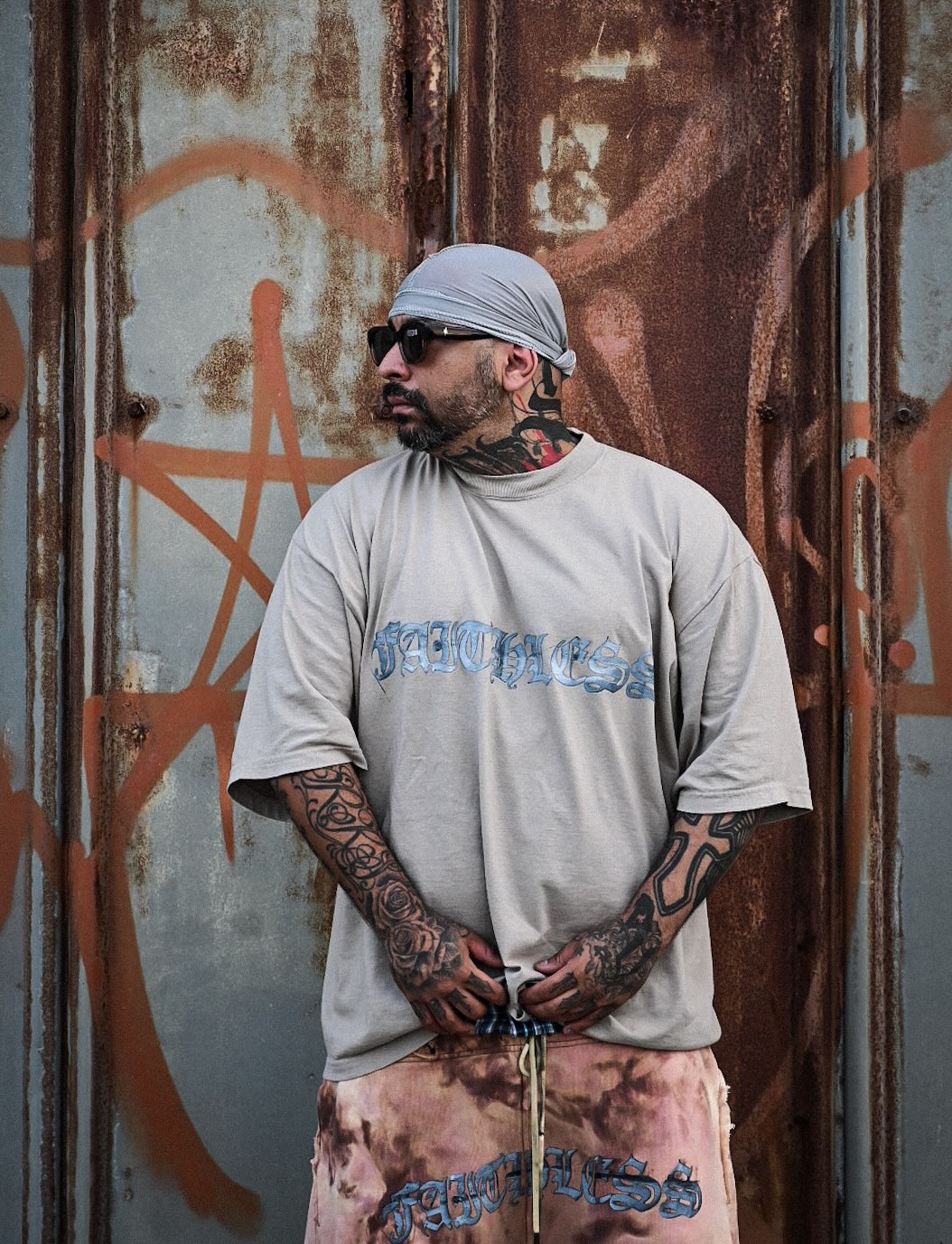 グラフィティ壁の前、タトゥーとFAITHLESSロゴTシャツ